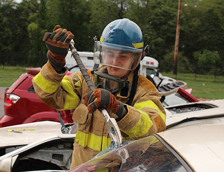 A medical student pries open a car windshield during the MFR Capstone event